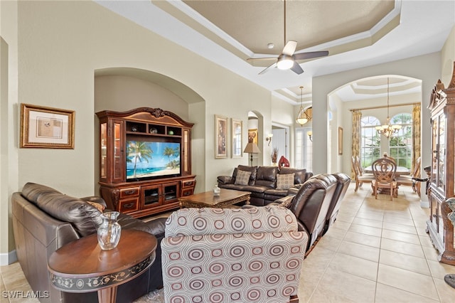 living room featuring ceiling fan with notable chandelier, ornamental molding, a raised ceiling, and light tile patterned flooring