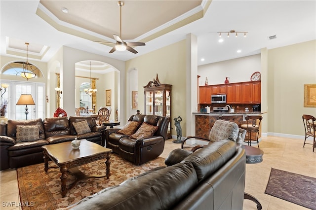 living room with ornamental molding, a tray ceiling, ceiling fan with notable chandelier, and light tile patterned floors