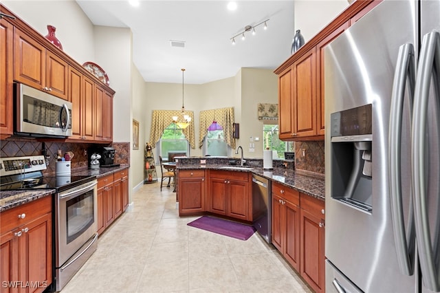 kitchen with sink, appliances with stainless steel finishes, light tile patterned flooring, decorative light fixtures, and dark stone counters