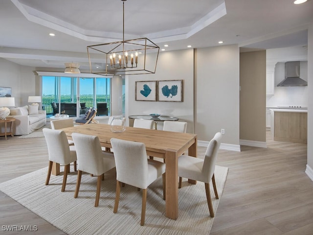 dining area featuring a notable chandelier, a tray ceiling, and light wood-type flooring