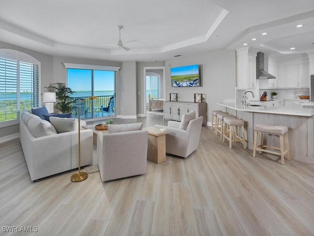 living room featuring light hardwood / wood-style flooring, ceiling fan, sink, and a raised ceiling