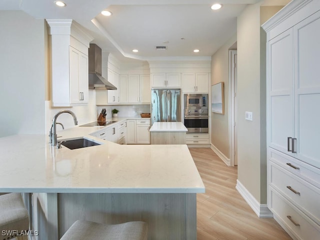 kitchen with sink, white cabinetry, stainless steel appliances, wall chimney exhaust hood, and light hardwood / wood-style flooring