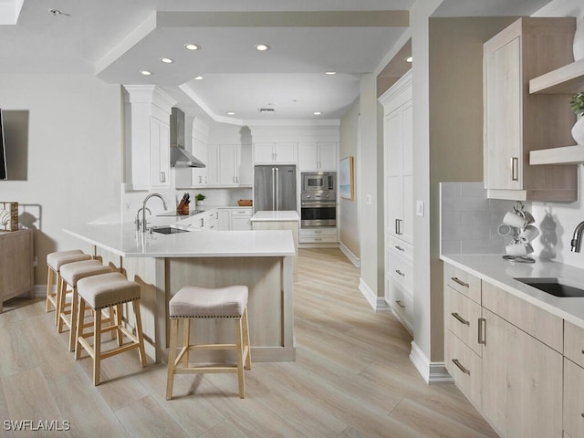 kitchen with a breakfast bar area, sink, appliances with stainless steel finishes, and wall chimney range hood