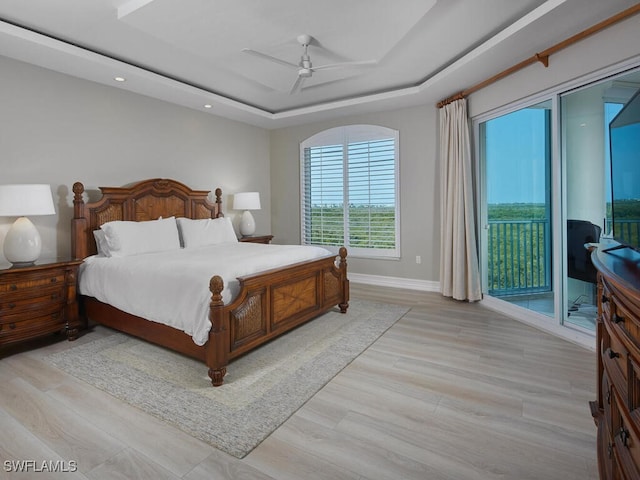 bedroom with light hardwood / wood-style floors, a tray ceiling, access to outside, and ceiling fan