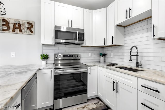 kitchen featuring appliances with stainless steel finishes, light stone countertops, sink, and white cabinets