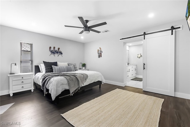 bedroom with a barn door, connected bathroom, dark wood-type flooring, and ceiling fan