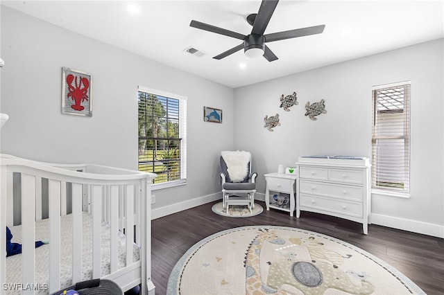 bedroom with ceiling fan, a crib, and dark hardwood / wood-style flooring