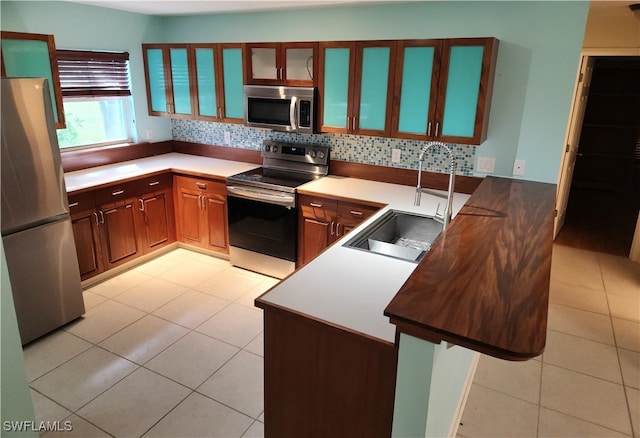 kitchen with tasteful backsplash, sink, kitchen peninsula, appliances with stainless steel finishes, and light tile patterned floors