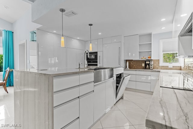 kitchen featuring white cabinetry, an island with sink, tasteful backsplash, light stone countertops, and pendant lighting