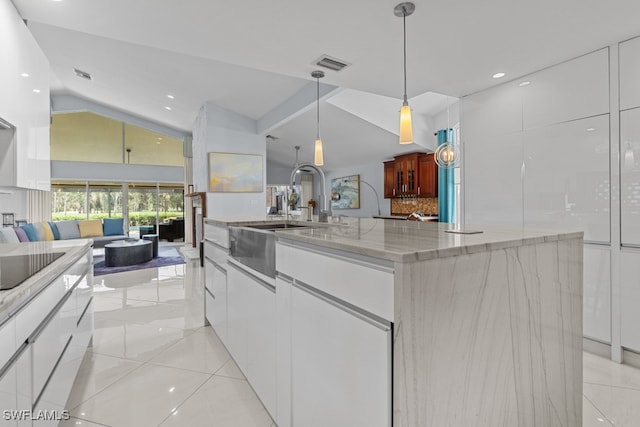 kitchen featuring light stone counters, white cabinets, sink, a large island with sink, and decorative light fixtures