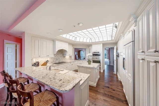 kitchen featuring kitchen peninsula, a center island, black electric cooktop, and light stone counters