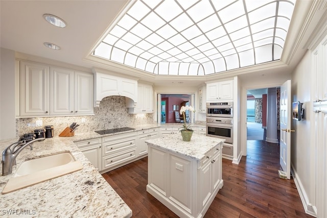 kitchen featuring premium range hood, light stone counters, black electric cooktop, sink, and white cabinetry