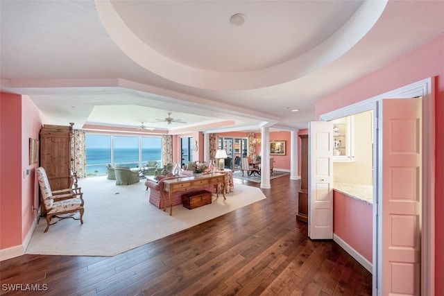 interior space featuring dark hardwood / wood-style floors, a water view, ornate columns, and a tray ceiling