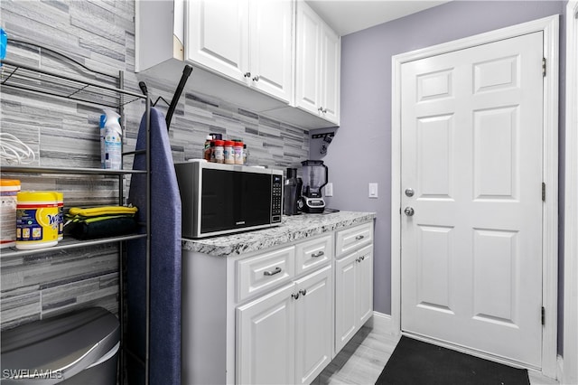 kitchen featuring white cabinetry, light stone counters, and tasteful backsplash