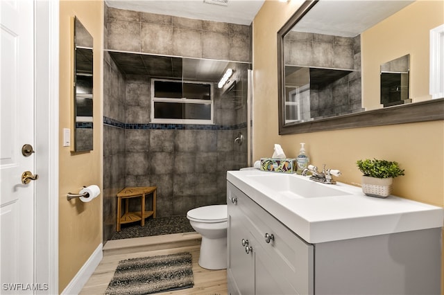 bathroom with vanity, hardwood / wood-style flooring, toilet, and a tile shower