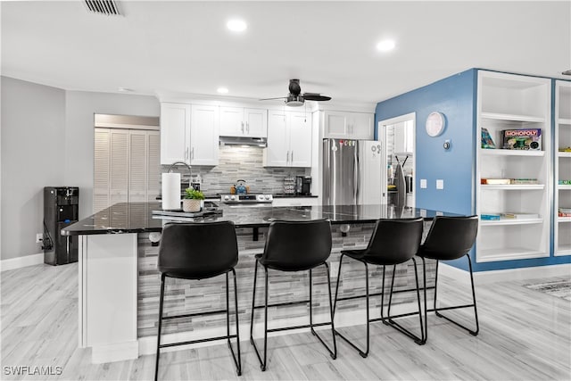 kitchen with appliances with stainless steel finishes, a kitchen island, a breakfast bar area, white cabinets, and light hardwood / wood-style flooring