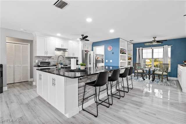 kitchen featuring stainless steel fridge, ceiling fan, white cabinets, light hardwood / wood-style flooring, and a kitchen island with sink