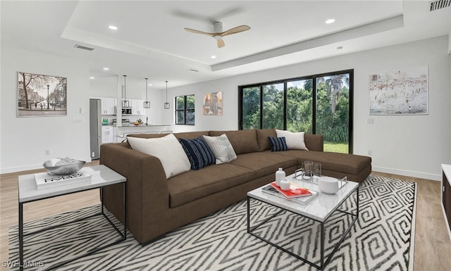 living room featuring a raised ceiling, ceiling fan, and light hardwood / wood-style flooring