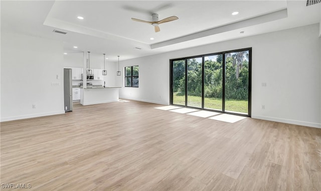 unfurnished living room featuring a raised ceiling, ceiling fan, and light wood-type flooring