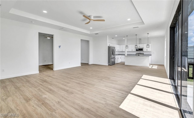 unfurnished living room with ceiling fan, a raised ceiling, and light wood-type flooring