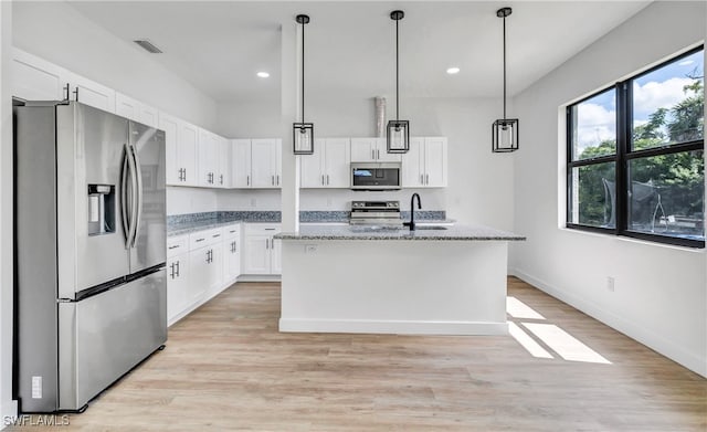 kitchen featuring stainless steel appliances, a kitchen island with sink, stone counters, light hardwood / wood-style floors, and white cabinetry