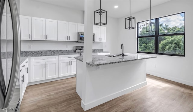 kitchen featuring appliances with stainless steel finishes, a kitchen island with sink, sink, white cabinetry, and hanging light fixtures