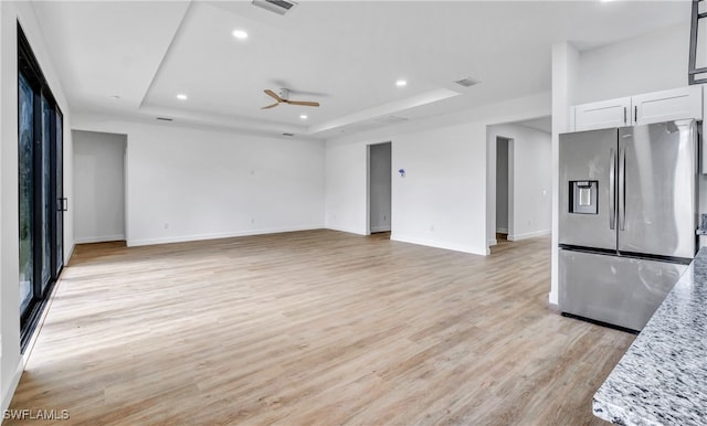 kitchen with white cabinetry, a raised ceiling, stainless steel fridge with ice dispenser, light stone counters, and light wood-type flooring