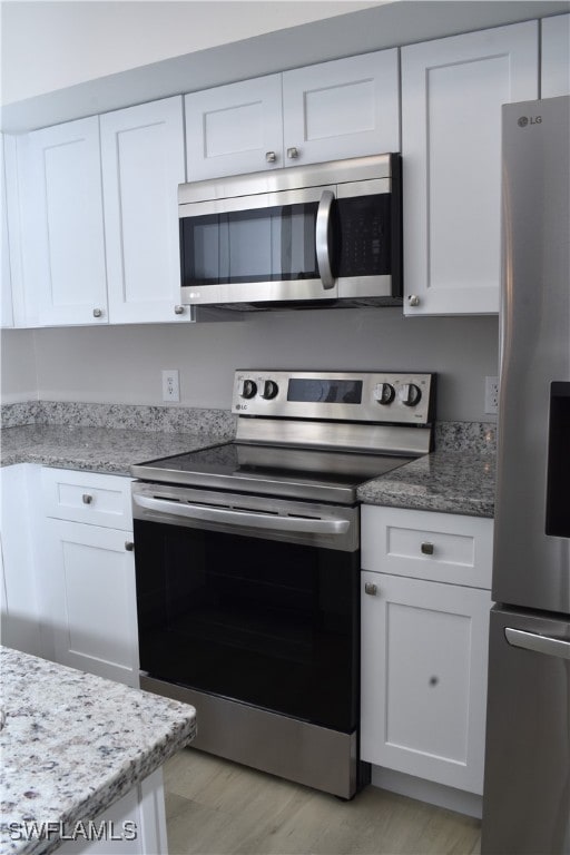 kitchen with light stone counters, light hardwood / wood-style floors, white cabinetry, and stainless steel appliances