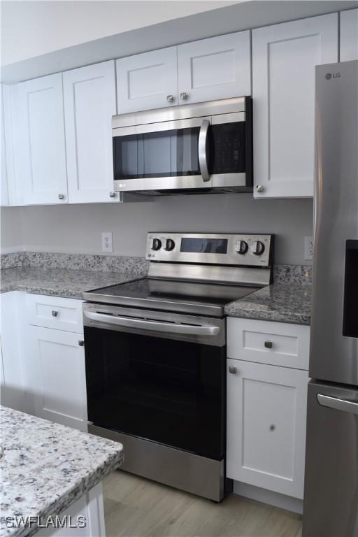 kitchen featuring white cabinetry, light hardwood / wood-style flooring, light stone countertops, and appliances with stainless steel finishes