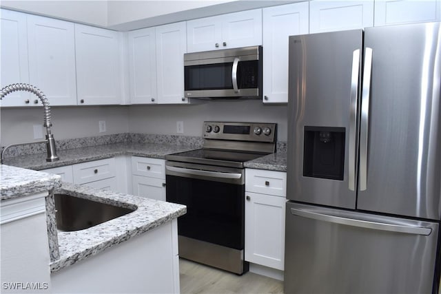 kitchen featuring light stone counters, light hardwood / wood-style flooring, stainless steel appliances, and white cabinetry