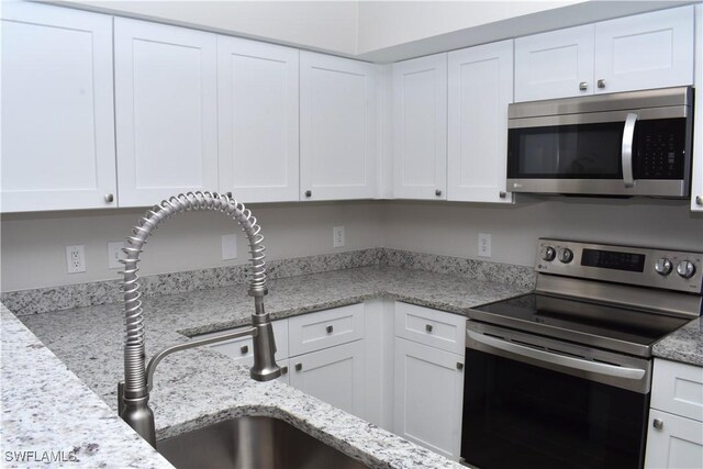 kitchen featuring light stone countertops, stainless steel appliances, and white cabinetry