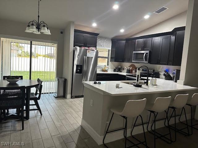 kitchen with light wood-type flooring, stainless steel appliances, sink, a notable chandelier, and lofted ceiling