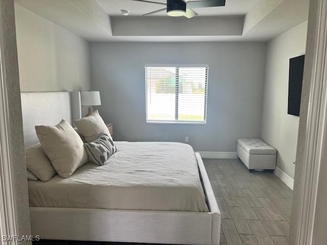 bedroom featuring ceiling fan, light hardwood / wood-style floors, and a raised ceiling