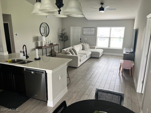 kitchen featuring ceiling fan, sink, stainless steel dishwasher, a breakfast bar area, and light wood-type flooring