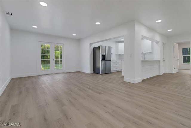 unfurnished living room featuring light wood-type flooring, sink, and french doors