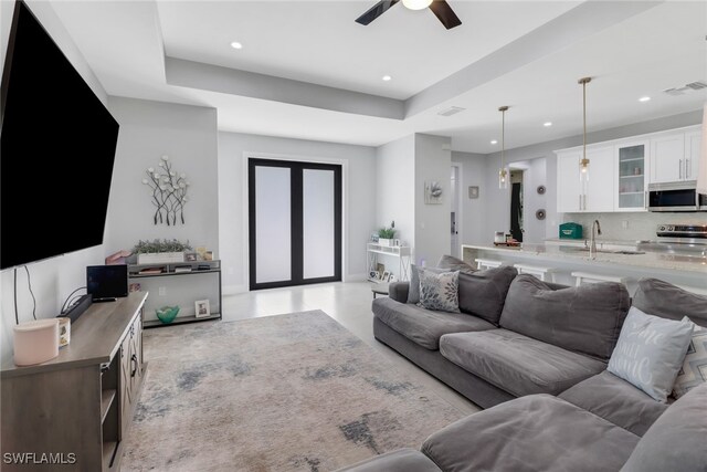 living room with a tray ceiling, ceiling fan, and sink