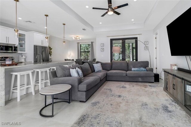 living room featuring ceiling fan, a raised ceiling, french doors, and sink