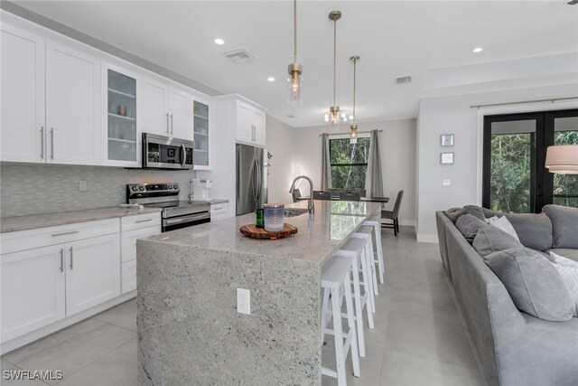 kitchen featuring appliances with stainless steel finishes, decorative backsplash, white cabinetry, an island with sink, and pendant lighting