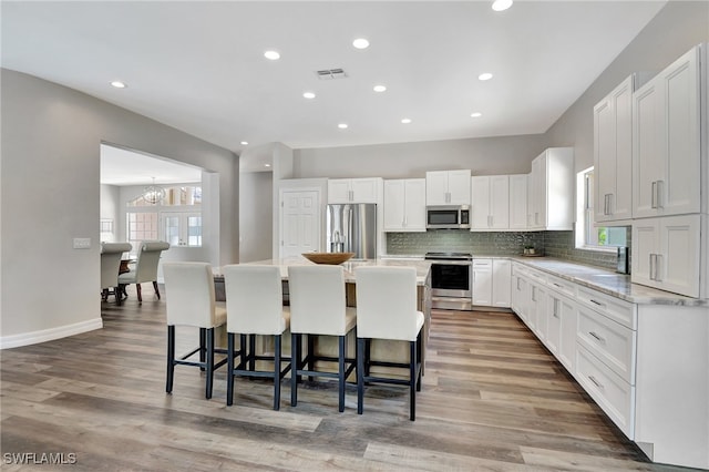 kitchen with white cabinets, stainless steel appliances, a kitchen breakfast bar, a center island, and hardwood / wood-style floors