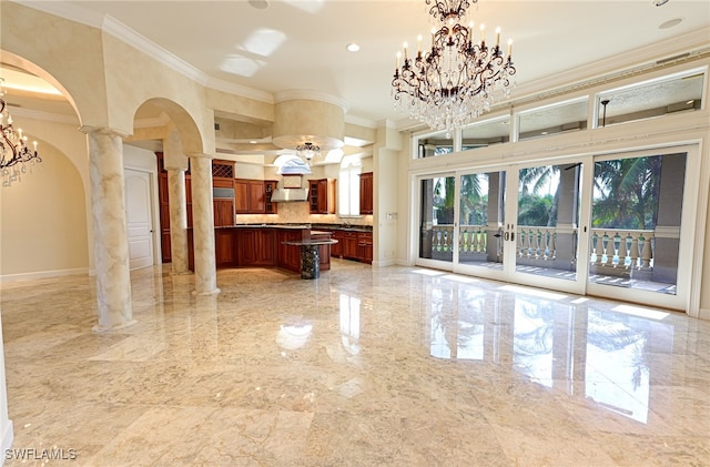 interior space with ornate columns, a center island, wall chimney exhaust hood, crown molding, and decorative light fixtures