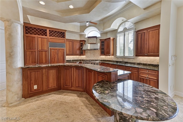 kitchen featuring dark stone counters, sink, decorative columns, a tray ceiling, and paneled refrigerator