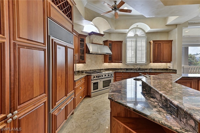 kitchen with dark stone countertops, wall chimney range hood, high quality appliances, and crown molding