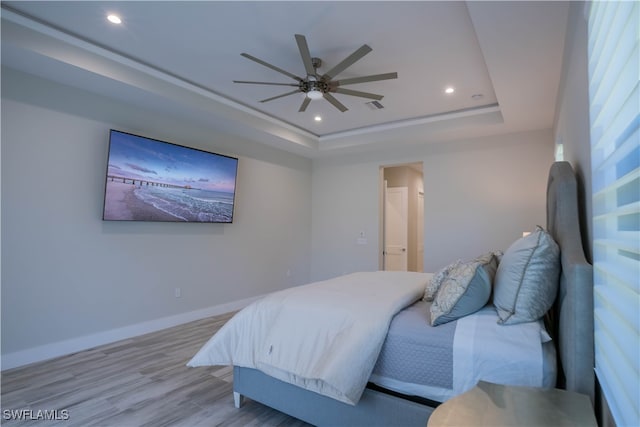 bedroom featuring ceiling fan, light wood-type flooring, and a raised ceiling