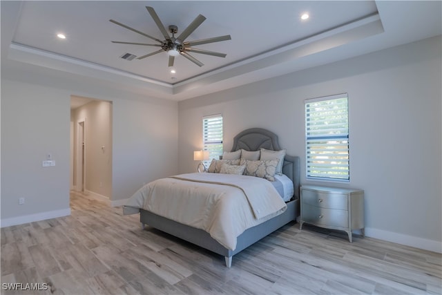 bedroom featuring ornamental molding, light wood-type flooring, a tray ceiling, and ceiling fan