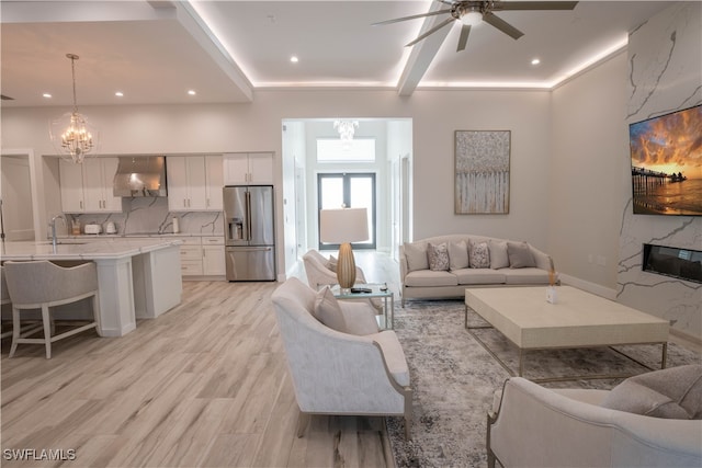 living room featuring ceiling fan with notable chandelier, light wood-type flooring, a premium fireplace, and sink