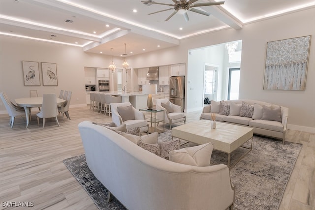 living room featuring ceiling fan with notable chandelier, beam ceiling, and light hardwood / wood-style flooring