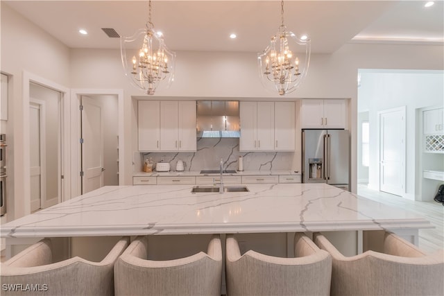 kitchen with white cabinets, a notable chandelier, high end fridge, and wall chimney range hood