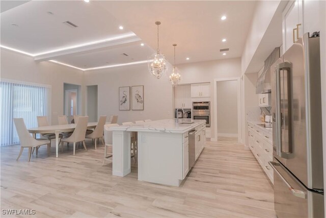 kitchen featuring white cabinets, a kitchen island with sink, light hardwood / wood-style flooring, appliances with stainless steel finishes, and a notable chandelier