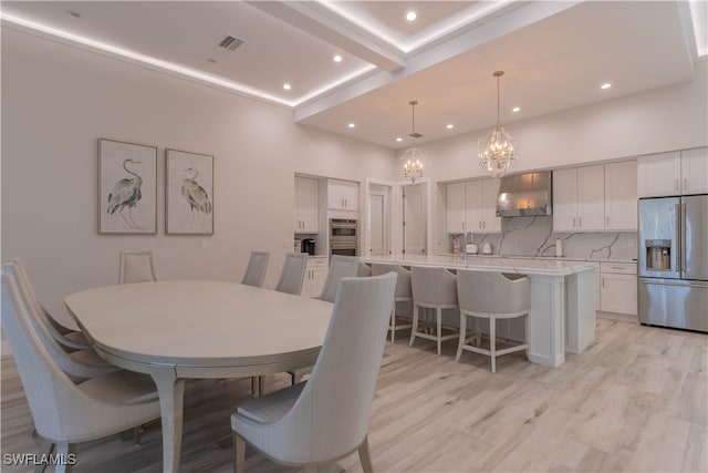 dining room featuring a towering ceiling, an inviting chandelier, and light hardwood / wood-style flooring