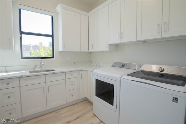 laundry room with cabinets, light hardwood / wood-style floors, sink, and washing machine and clothes dryer